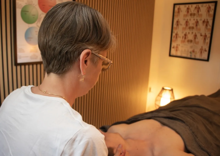 Zarah fra Nakskov Kropsterapi i gang med behandling i klinikrum med rolig belysning og anatomiplakat